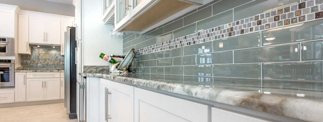 White shaker cabinets featuring a glass subway tile backsplash with tile insert, granite countertops and modern stainless steel pulls