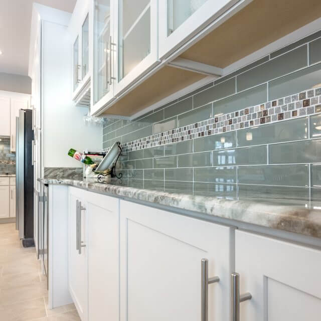 White shaker cabinets featuring a glass subway tile backsplash with tile insert, granite countertops and modern stainless steel pulls